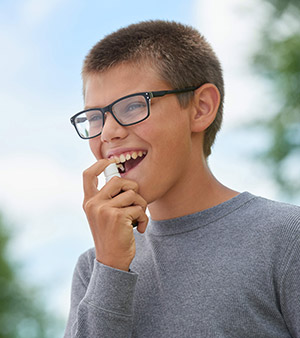 Boy with glasses administering allergy drops to himself outside